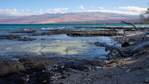 Una costa rocosa con aguas cristalinas y una montaña al fondo.