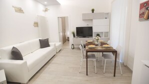 A modern living room with a white sofa, a dining table set for four, and a TV mounted above it.