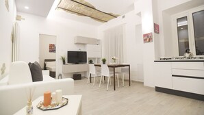 A modern living room with a sofa, a dining table with chairs, a TV, and a kitchen area with a stove.