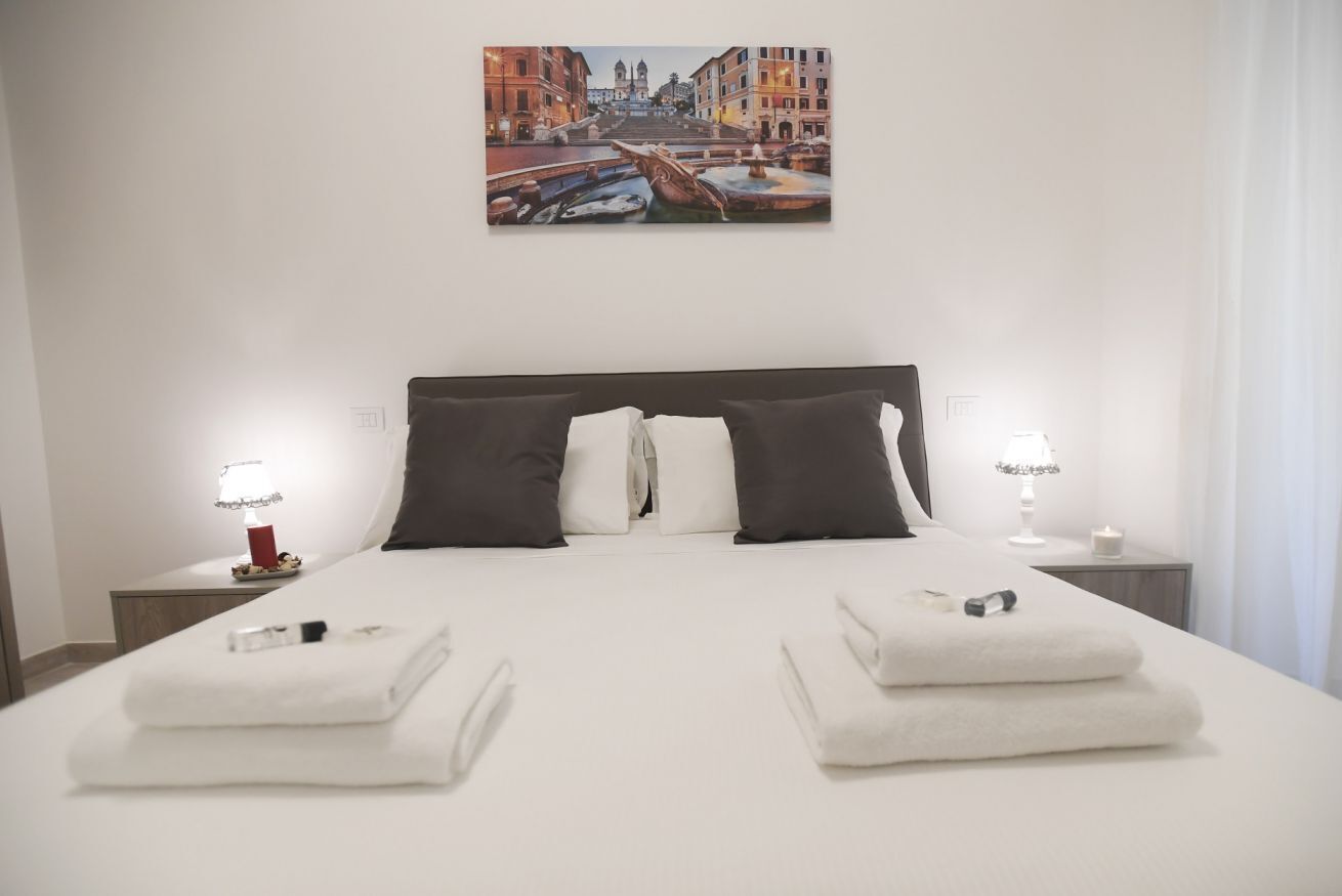 A hotel room with a large bed, two bedside tables, a painting of a cityscape, and a view of the city.