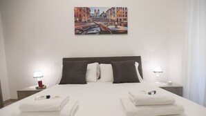 A hotel room with a large bed, two bedside tables, a painting of a cityscape, and a view of the city.