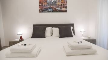 A hotel room with a large bed, two bedside tables, a painting of a cityscape, and a view of the city.
