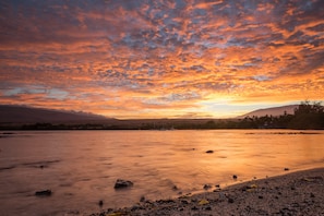 A river at sunset with boats, a rocky shoreline, and distant mountains.