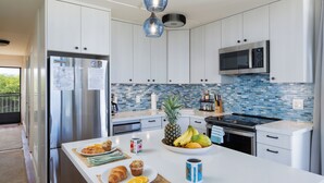 Een moderne keuken met witte kasten, een roestvrijstalen koelkast, een magnetron en een betegelde spatwand.