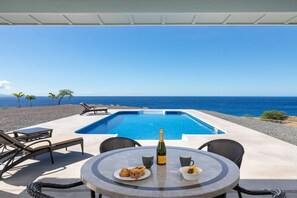 A poolside area with a table set for two, a bottle of champagne, and a plate of food. - B.I. Kohola Lani , Very private, Pool, Amazing Views! AC in bedrooms! (Kamuela)