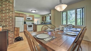 A dining area with a wooden table set for four, a brick wall, and a kitchen in the background.