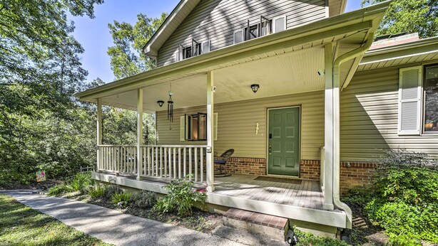 A two-story house with a covered porch, a green door, and a brick foundation.