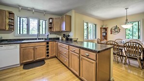 A kitchen with wooden cabinets, a dishwasher, a granite countertop, and a dining area with wooden chairs and a table.