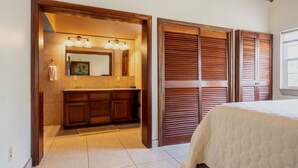 Ein Schlafzimmer mit Bett, Holztüren zu einem Kleiderschrank und einem Badezimmer mit Waschbecken und Spiegel.