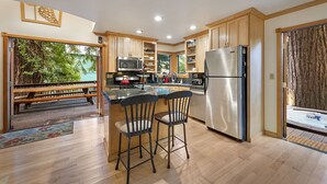 Une cuisine moderne dotée de meubles en bois, d’appareils électroménagers en acier inoxydable et d’un coin bar avec deux tabourets.