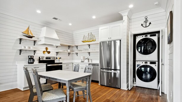 A modern kitchen with white cabinetry, stainless steel appliances, and a dining area with a wooden table and chairs. - New 2 Bedroom Beach Rental in downtown Bay St Louis (Bay St. Louis)
