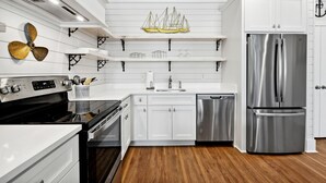 A modern kitchen with white cabinetry, stainless steel appliances, and a wooden floor. - New 2 Bedroom Beach Rental in downtown Bay St Louis (Bay St. Louis)