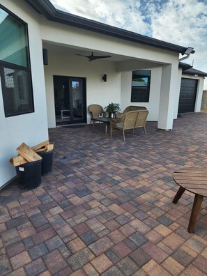 Een overdekt terras met een tafel, stoelen, een plafondventilator en een garagepoort.