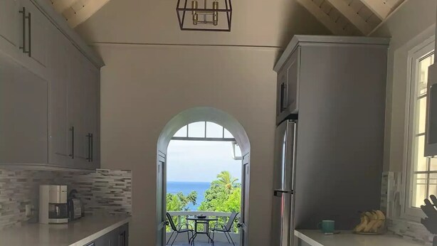 Eine moderne Küche mit Blick auf einen Balkon, ausgestattet mit Edelstahlgeräten, einer Hängeleuchte und einem gefliesten Boden.