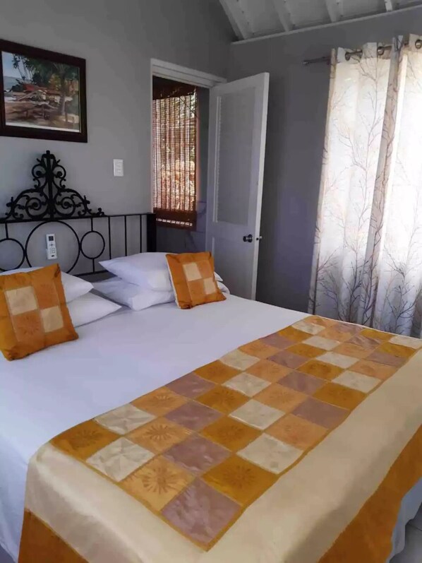A bed with a checkered bedspread, two pillows, a wall-mounted phone, a painting, and a window with blinds.