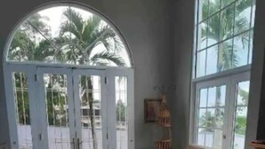 Ein großzügiger Wohnraum mit einem großen Bogenfenster, einem Sofa mit bunten Kissen, einem Korbstuhl und einem Holztisch.