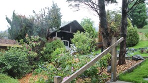 Eine hölzerne Treppe führt zu einem Haus, das von üppigem Grün und einem Garten umgeben ist.