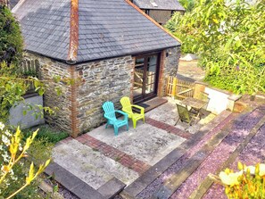 A stone building with a tiled roof, a small patio with two chairs, and a wooden table. - Threpney Cottage-UK12898 (Pelynt, near Looe)
