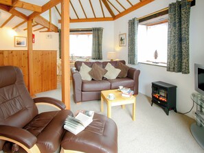 A cozy living room with a leather sofa, a wooden coffee table, a fireplace, and a television. - Threpney Cottage-UK12898 (Pelynt, near Looe)