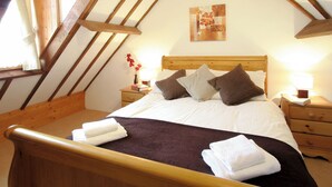 A bedroom with a wooden headboard, a bed with white and brown bedding, two bedside tables with lamps, and a painting on the wall.