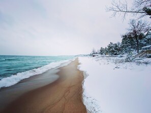 A beach with snow-covered trees and a wooden structure on the right.