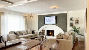 A cozy living room with a fireplace, comfortable seating, and a television mounted above it. - Summer Getaway - 3 min walk to Beach, Clean & Cozy (Tiny)