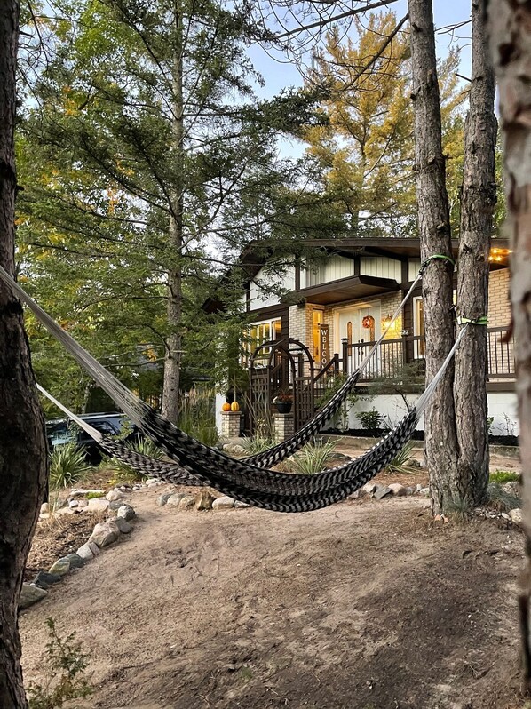A hammock in a wooded area with a building in the background.