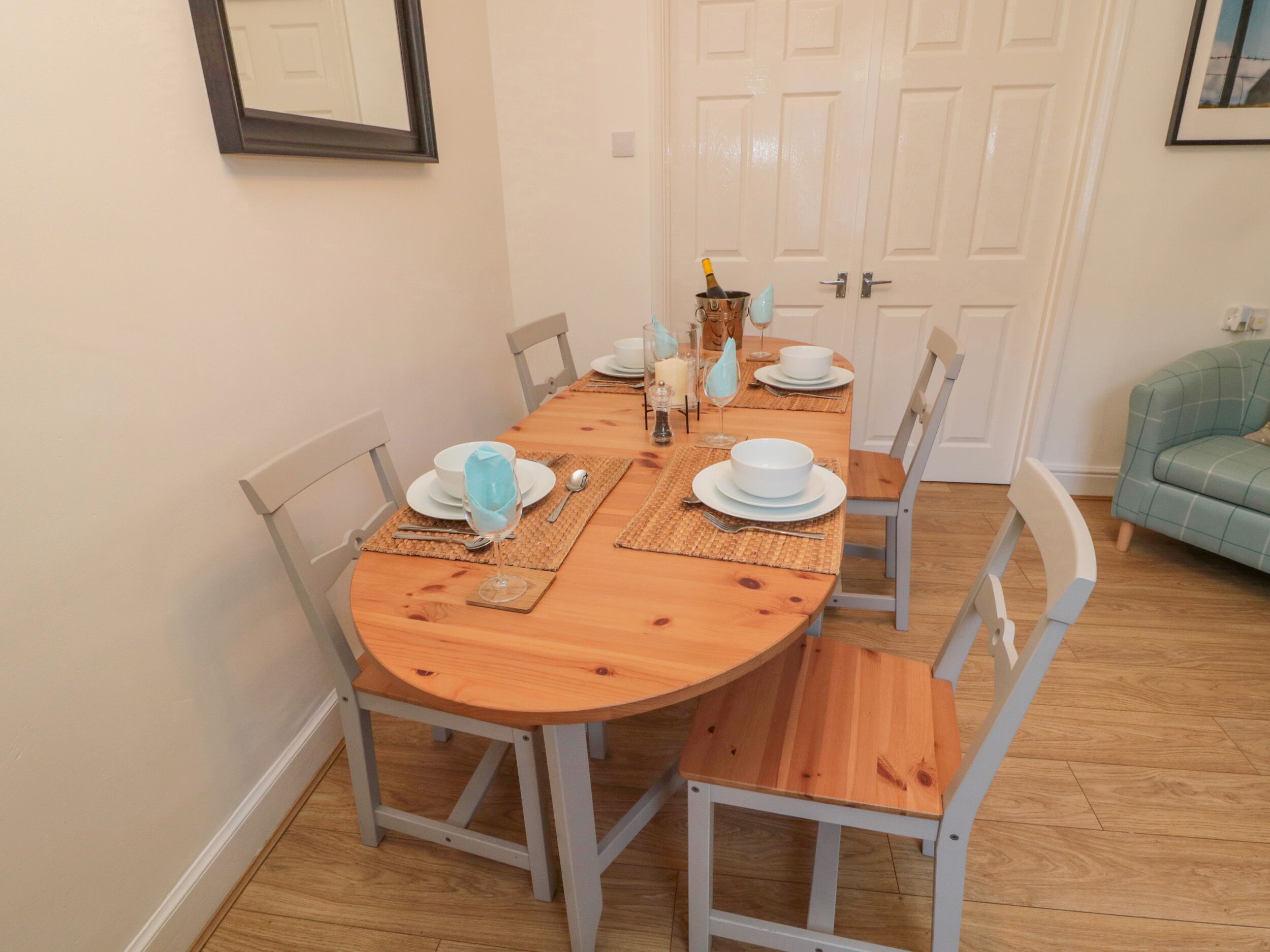 A dining room with a wooden table set for four, surrounded by four chairs.