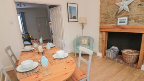 A dining area with a wooden table set for four, white chairs, and a stone fireplace with a star decoration. - Redshank (Morpeth)