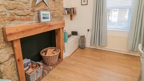 A cozy room with a stone fireplace, a wooden mantel, and a star decoration. There is a basket of firewood, a wicker basket, and a small shelf with books. - Redshank (Morpeth)