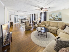 A spacious living room with a sofa, armchairs, a coffee table, and a television.