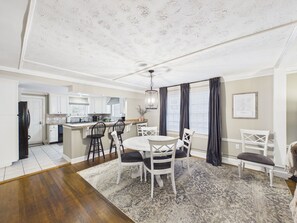 A modern kitchen with white cabinets, a dining area with a round table and chairs, and a large window with curtains.