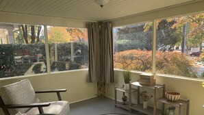 A cozy room with a view of autumn trees, a chair, a small table with a plant, and a decorative bowl. - Cozy Cottage on Canton Street just steps away from nightlife, shopping and parks (Roswell)
