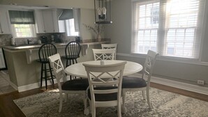 A dining area with a round table and chairs, a kitchen in the background, and a large window with blinds. - Cozy Cottage on Canton Street just steps away from nightlife, shopping and parks (Roswell)
