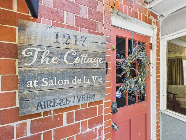 Un cartello di legno con l'indirizzo '1217 The Cottage at Salon de la Vie' e il logo AirBnB.