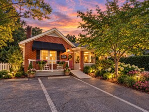 A brick building with a black awning, a porch with chairs, and a sign that reads 'The Cottage.'