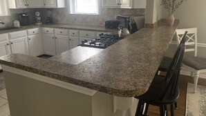 A kitchen with white cabinets, a granite countertop, a gas stove, and a window with blinds. - Cozy Cottage on Canton Street just steps away from nightlife, shopping and parks (Roswell)