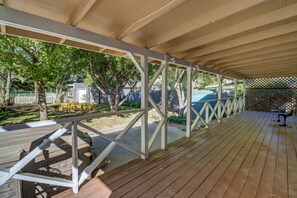 Una terraza cubierta al aire libre con barandilla, piso de madera y vista a un jardín trasero con árboles y una cerca.