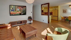 Een moderne woonkamer met een houten salontafel, een aan de muur bevestigde televisie, en een eethoek met gele stoelen.