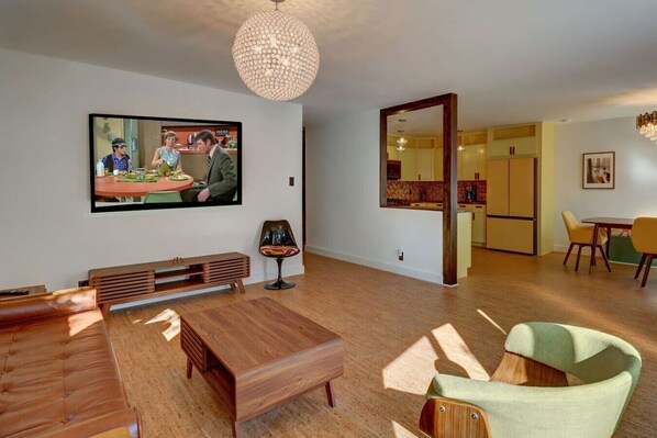 Una sala de estar moderna con una mesa de centro de madera, un televisor montado en la pared y un comedor con sillas amarillas.