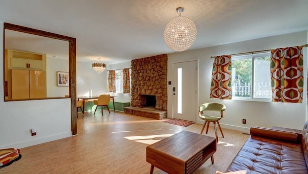 Een ruime woonkamer met een open haard, een eethoek en een groot raam met gordijnen.