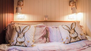 Un dormitorio con una cama que incluye almohadas con motivos de conejo, un cabecero de madera y lámparas fijadas a la pared.