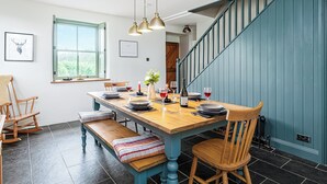 A dining area with a wooden table, benches, and hanging pendant lights. - An impressive, detached stone-built cottage set within Gwydir Forest. (Betws-y-Coed)