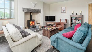 A cozy living room with a fireplace, a television, and comfortable seating. - An impressive, detached stone-built cottage set within Gwydir Forest. (Betws-y-Coed)