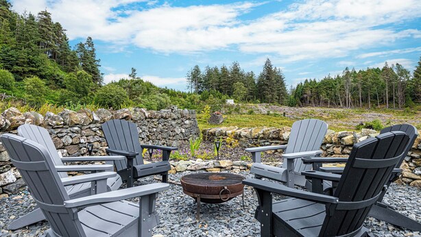 A stone wall, a fire pit, and four Adirondack chairs arranged around it. - An impressive, detached stone-built cottage set within Gwydir Forest. (Betws-y-Coed)