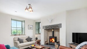 A cozy living room with a fireplace, a sofa, a coffee table, and a television. - An impressive, detached stone-built cottage set within Gwydir Forest. (Betws-y-Coed)