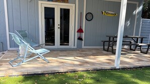 Een overdekt terras met een bord van een tiki bar, een Corona-bord, een picknicktafel en een ligstoel bij het zwembad.