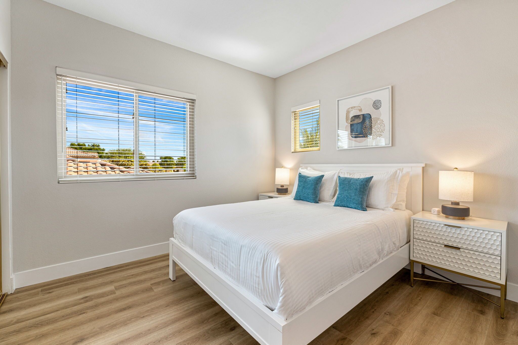 A bedroom with a large bed, two bedside tables, a nightstand, and a window with blinds.