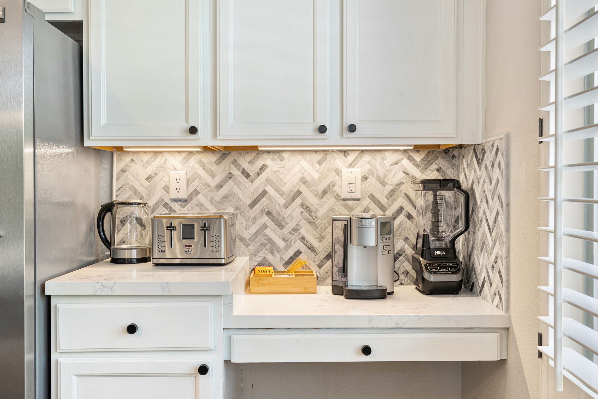 A kitchen with white cabinets, a marble countertop, a coffee maker, a toaster, and a blender.