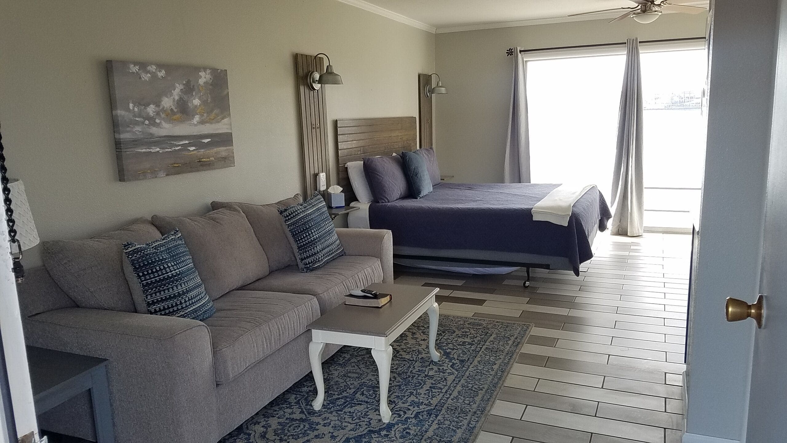 A bedroom with a bed, a sofa, a bedside table, a lamp, and a painting on the wall.